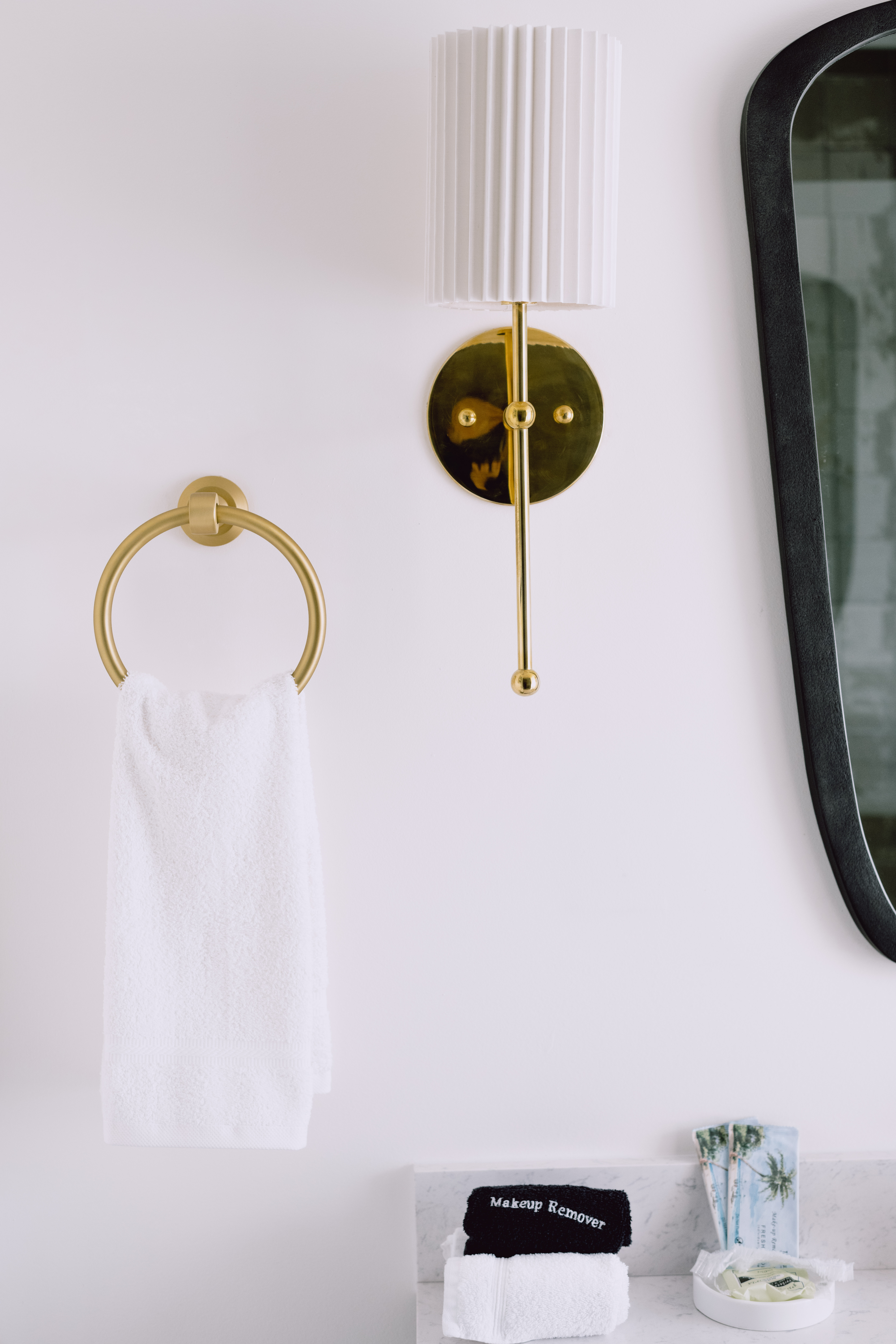 An image of a towel hook with a white towel, a sconce on a white wall, and part of a mirror