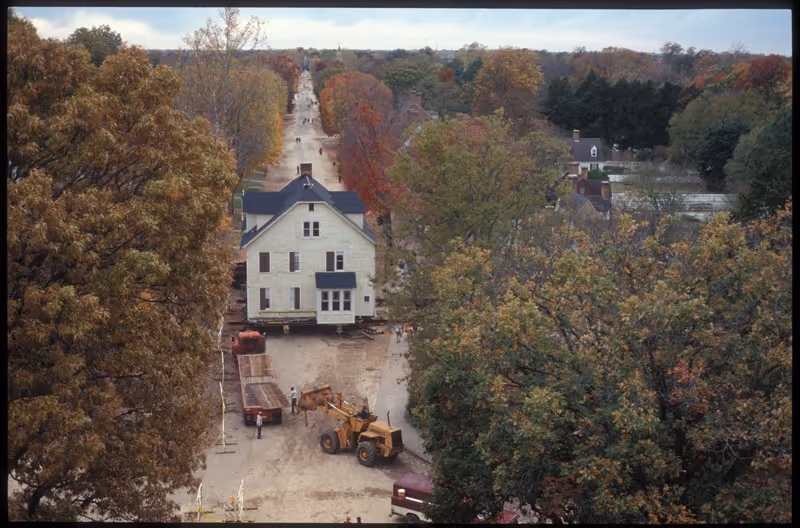 Aerial view from the Capitol building cupola in Colonial Williamsburg showing the Armistead House being transported down Duke of Gloucester Street during its 1995 relocation, flanked by fall foliage