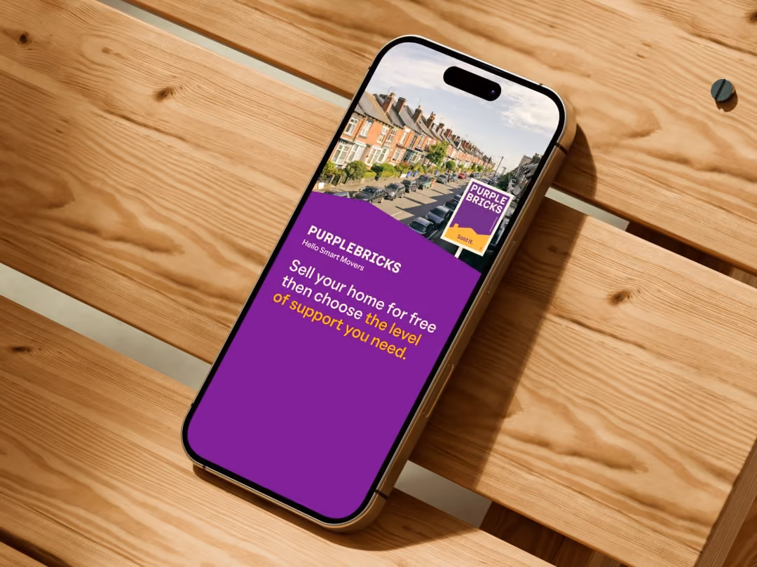 Smartphone on wooden surface showing Purplebricks ad about selling homes for free with support options.