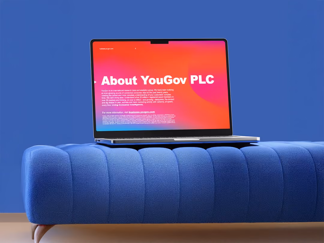 Laptop on blue cushioned bench displaying a red and pink screen with white text about YouGov PLC.