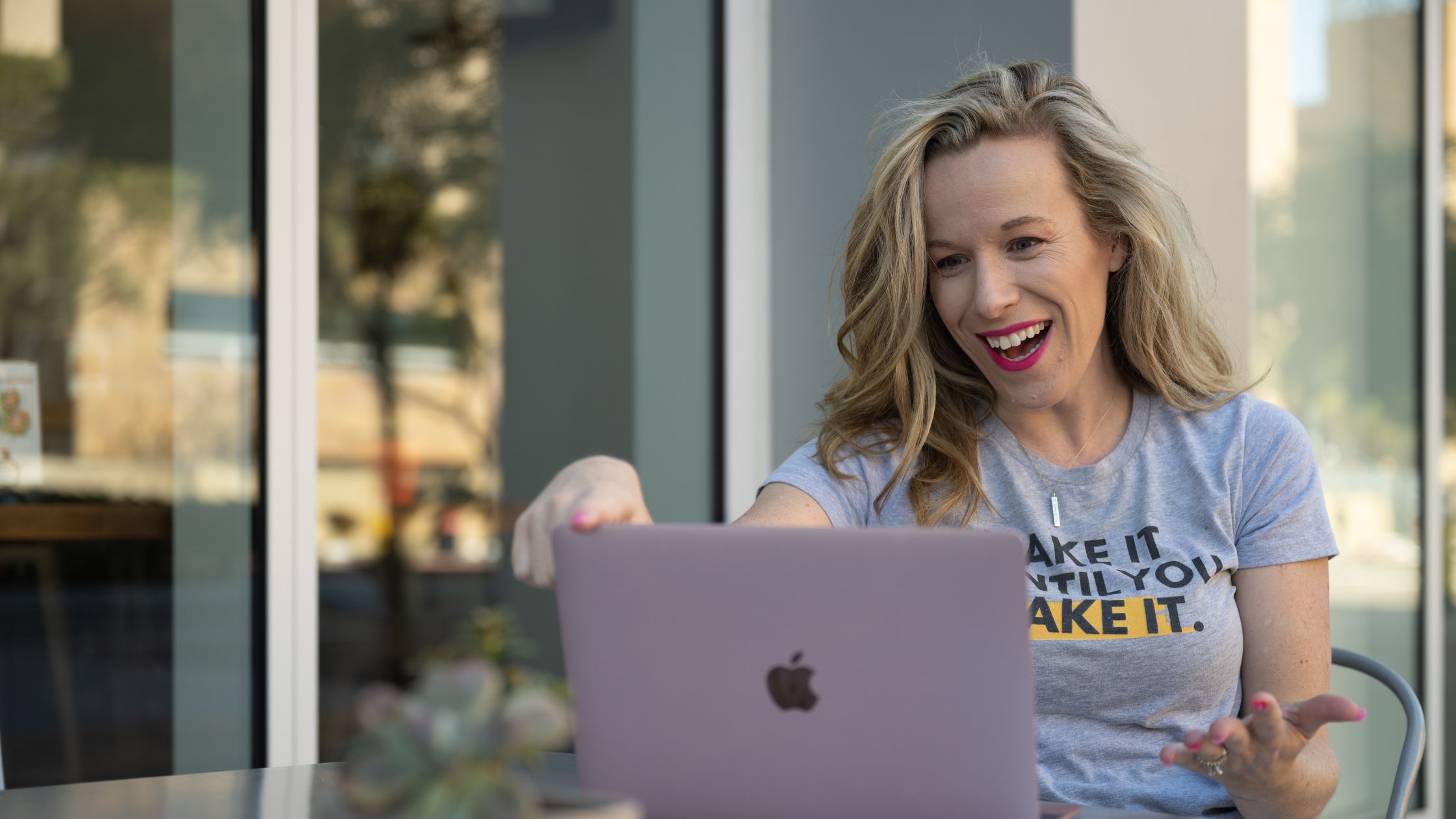 Kelly Mirabella sitting at a cafe table outside working on her laptop