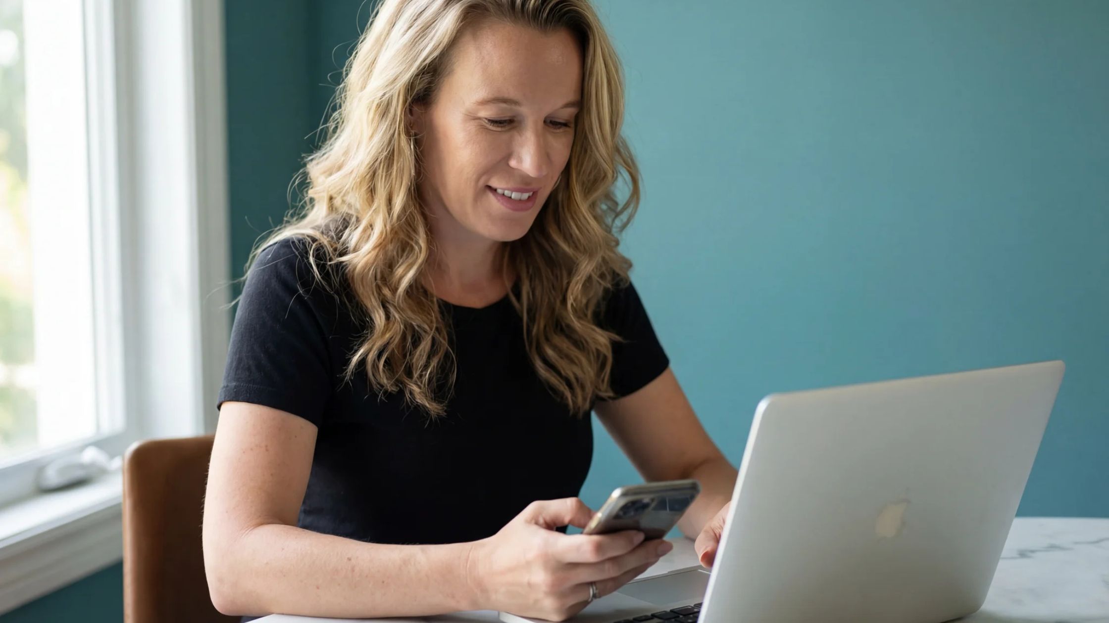 Kelly Mirabella working with a phone in one hand and her laptop in front of her
