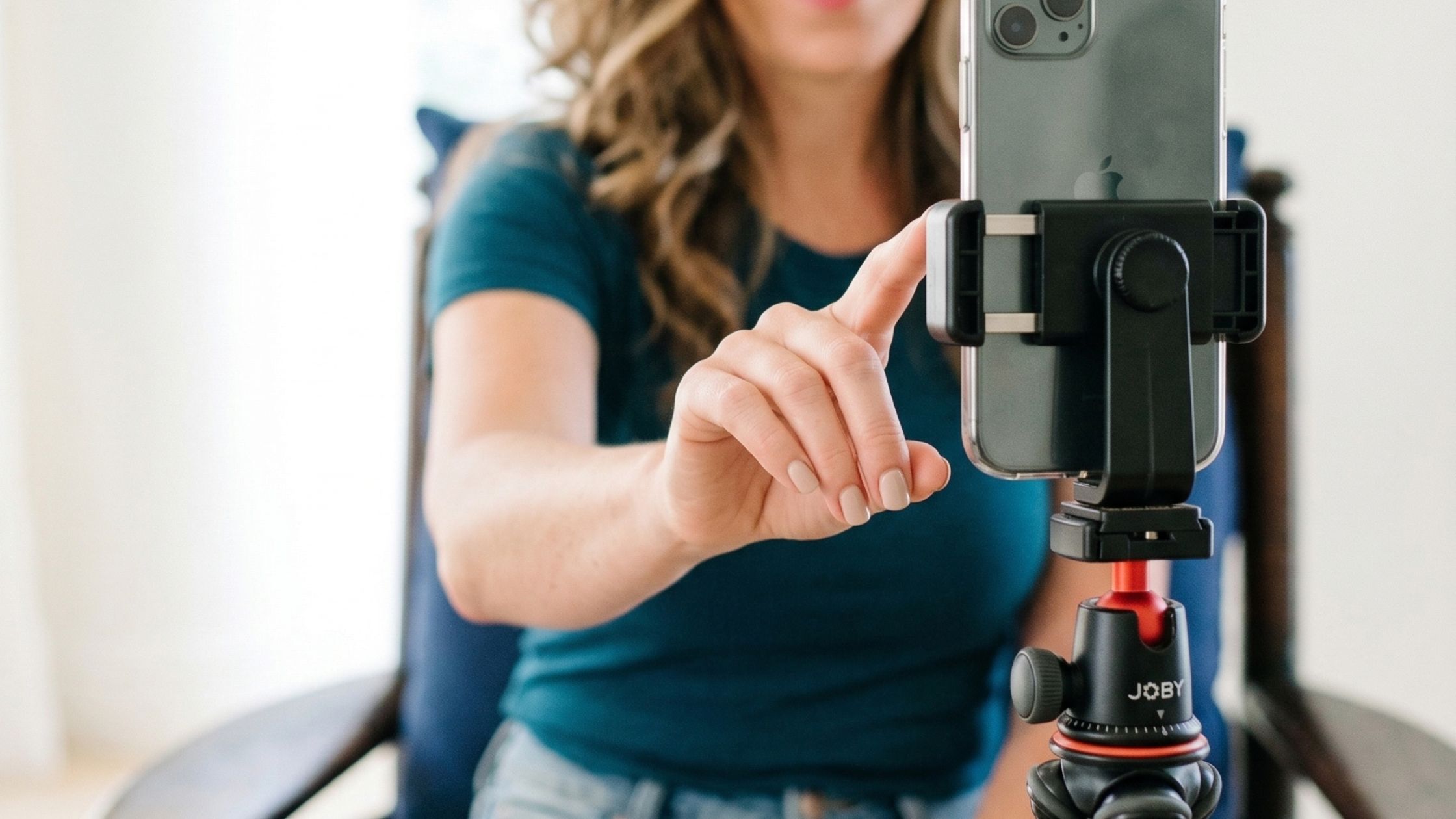 A woman pushing a button on her phone which is attached to a tripod