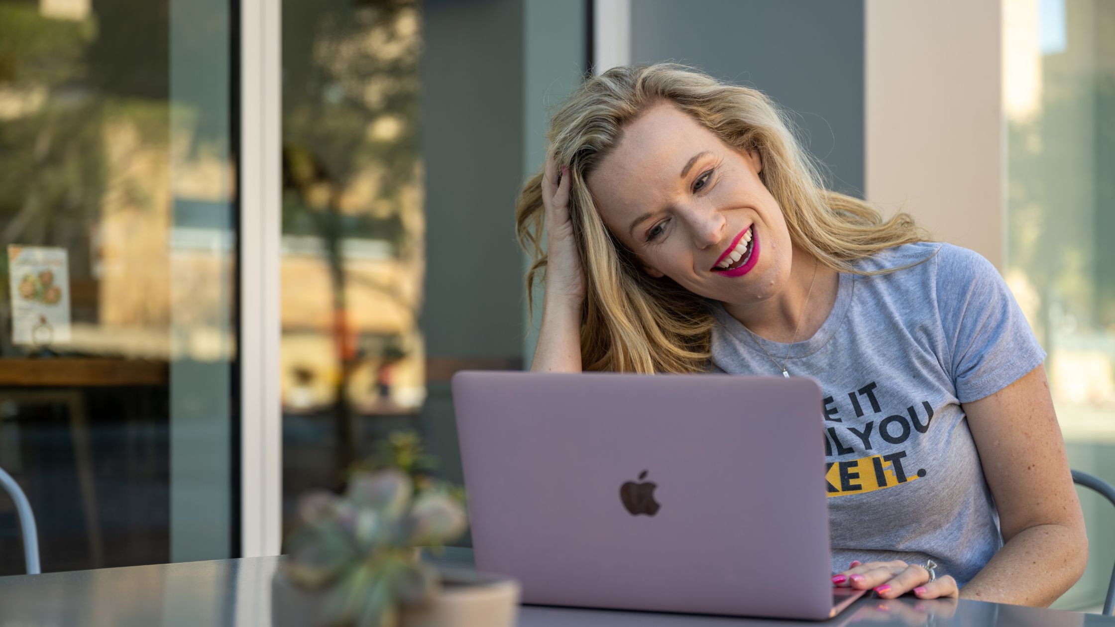 Kelly Mirabella sitting at a table outside smiling at her taptop screen
