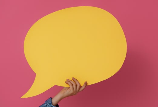 Yellow speech bubble being held in front of a pink background