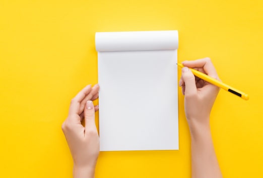 Someone holding a blank notebook and a yellow pencil