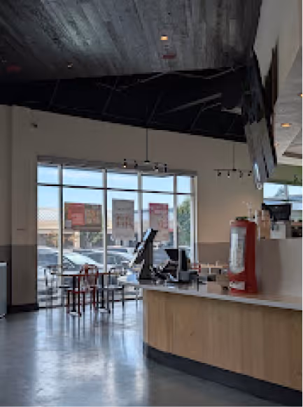 Interior of a modern café with a wooden counter, digital registers, and seating near large windows showing parked cars outside.