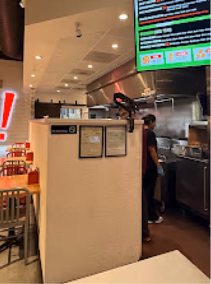 Interior view of a restaurant kitchen area with a worker cooking and tables with chairs in the dining area.