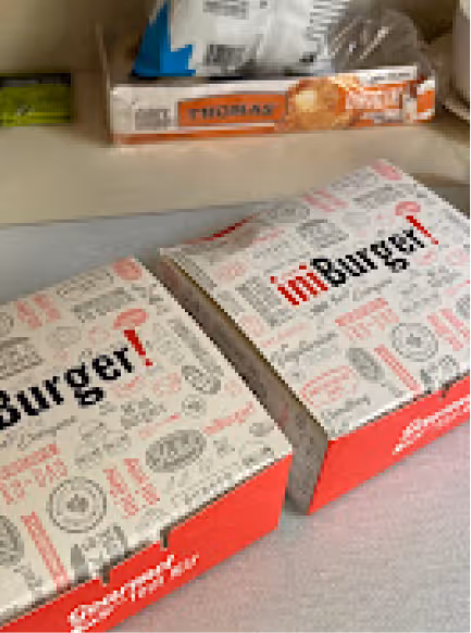 Two closed imBurger takeout boxes with white lids printed with various food-related icons and the red logo on a white surface.