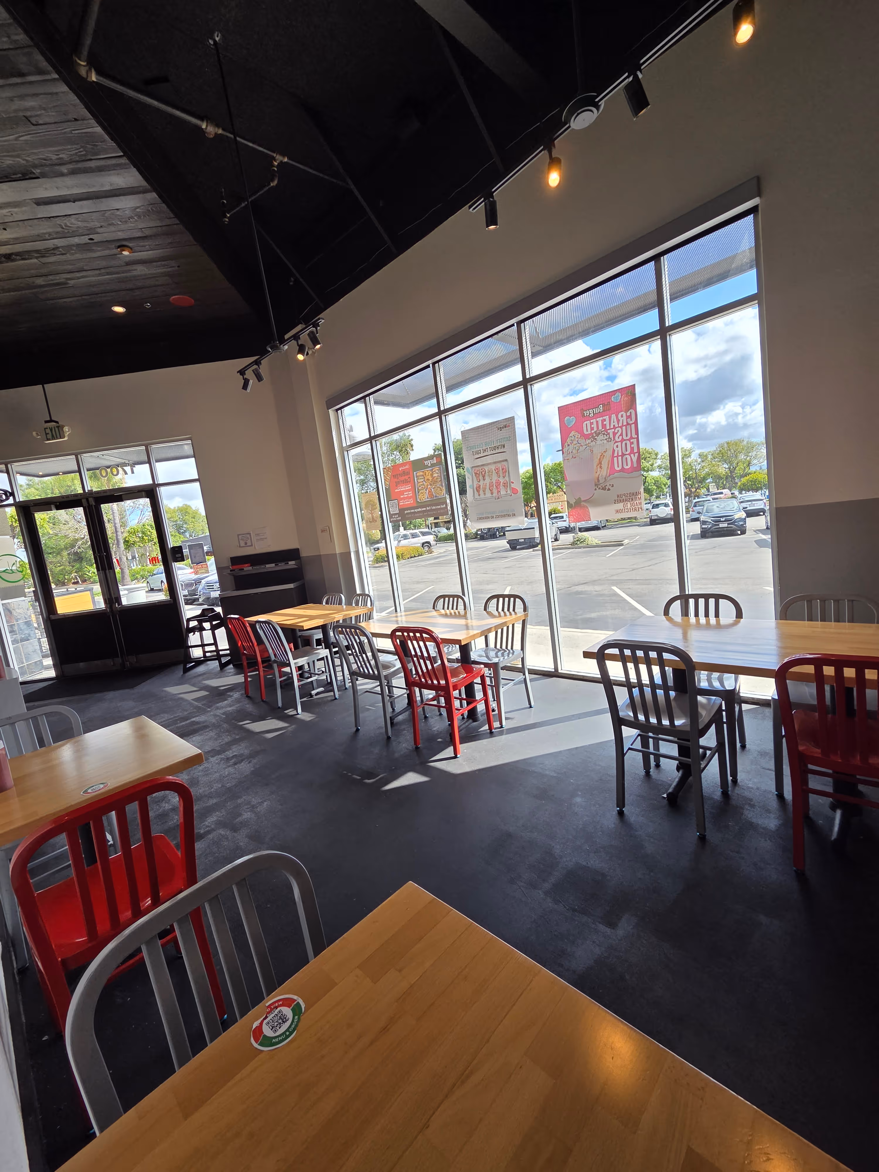 Interior of a modern café with a wooden counter, digital registers, and seating near large windows showing parked cars outside.