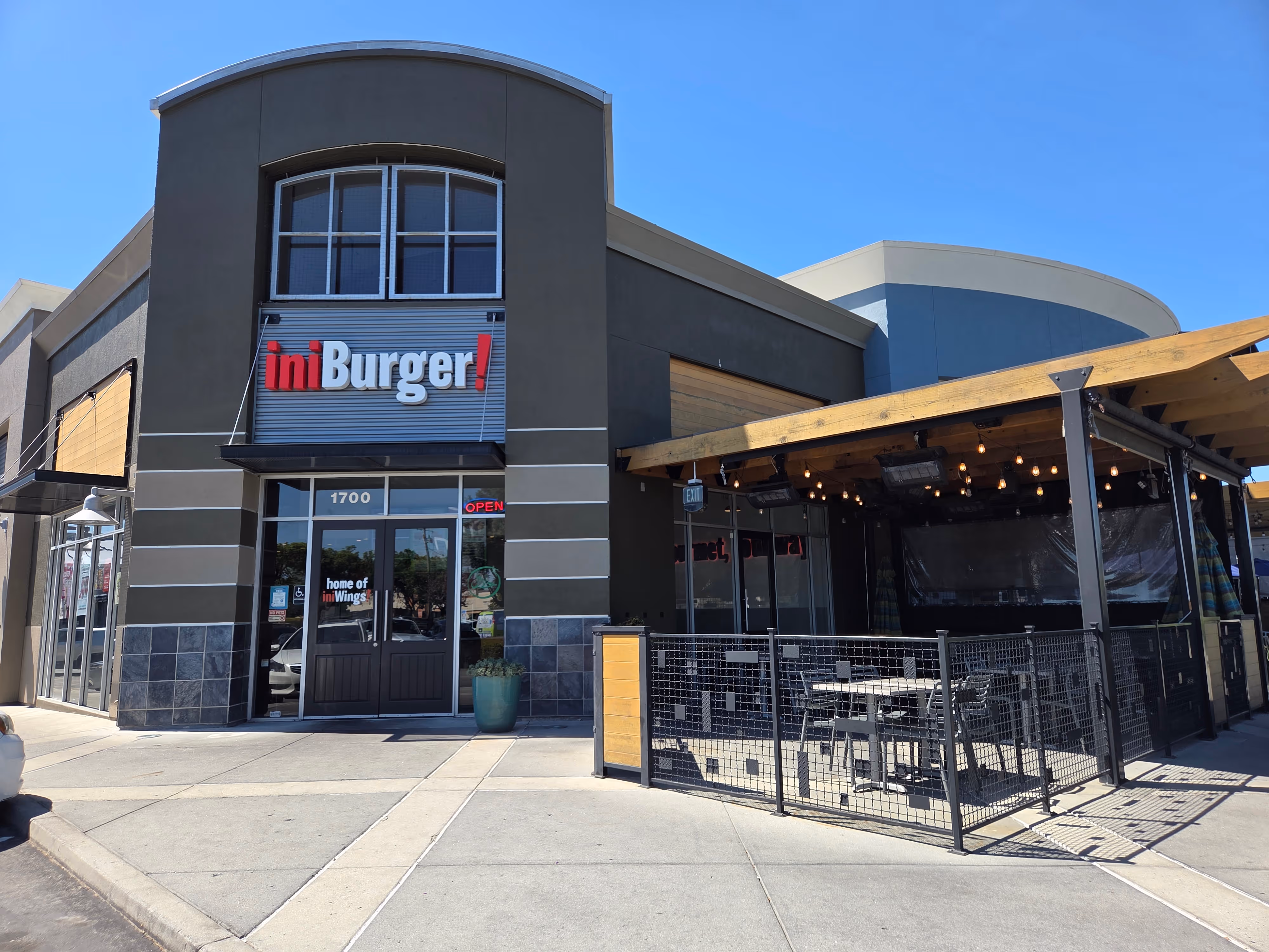Exterior of iniBurger restaurant with glass entrance, two blue planters, under clear blue sky.