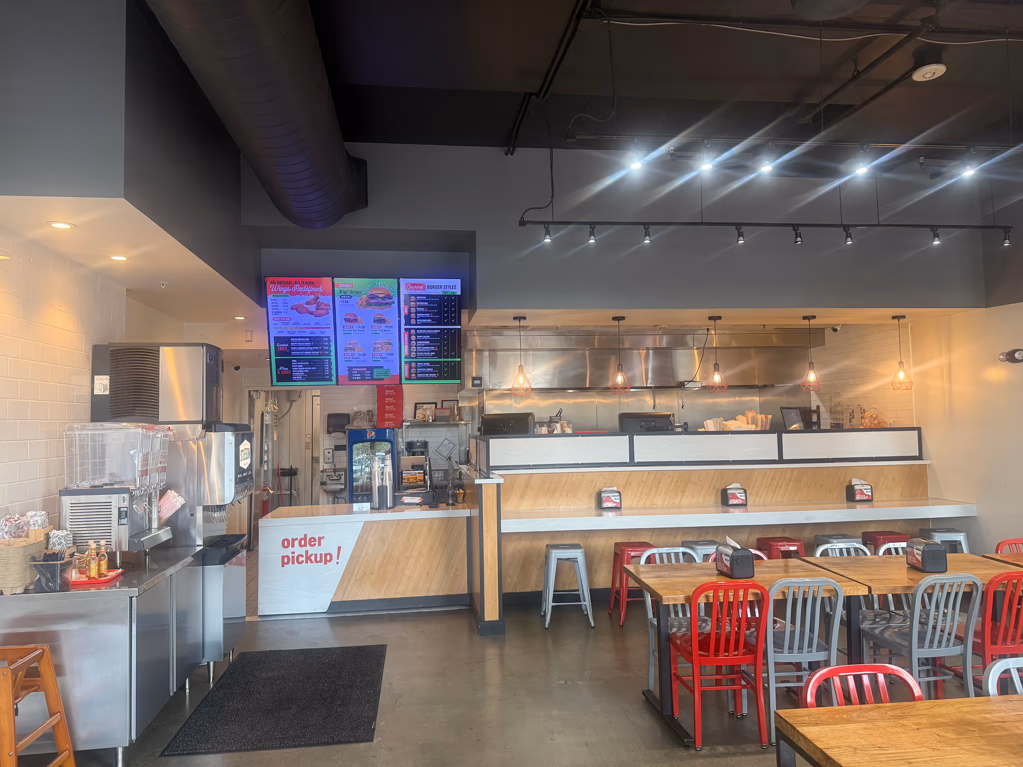Interior view of a restaurant kitchen area with a worker cooking and tables with chairs in the dining area.