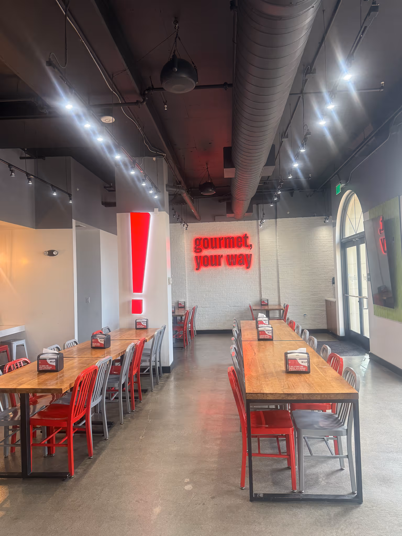 Interior of a modern café with a wooden counter, digital registers, and seating near large windows showing parked cars outside.