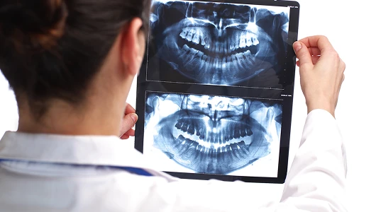 Dentist viewing two panoramic dental X-rays on a tablet screen. Bright, high-contrast studio lighting against a clean white background.