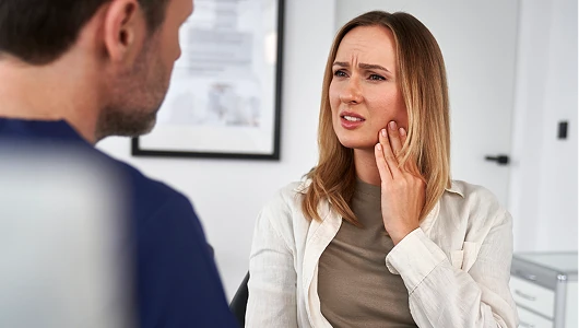 Patient with tooth pain consulting a dentist in a bright, modern clinic. The woman touches her cheek with a concerned expression during the visit.