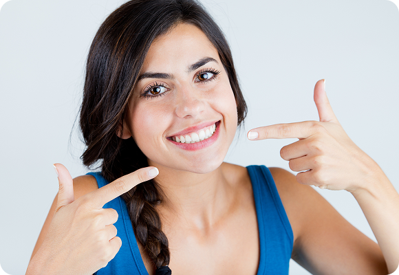 A girl smiling, pointing to her smile
