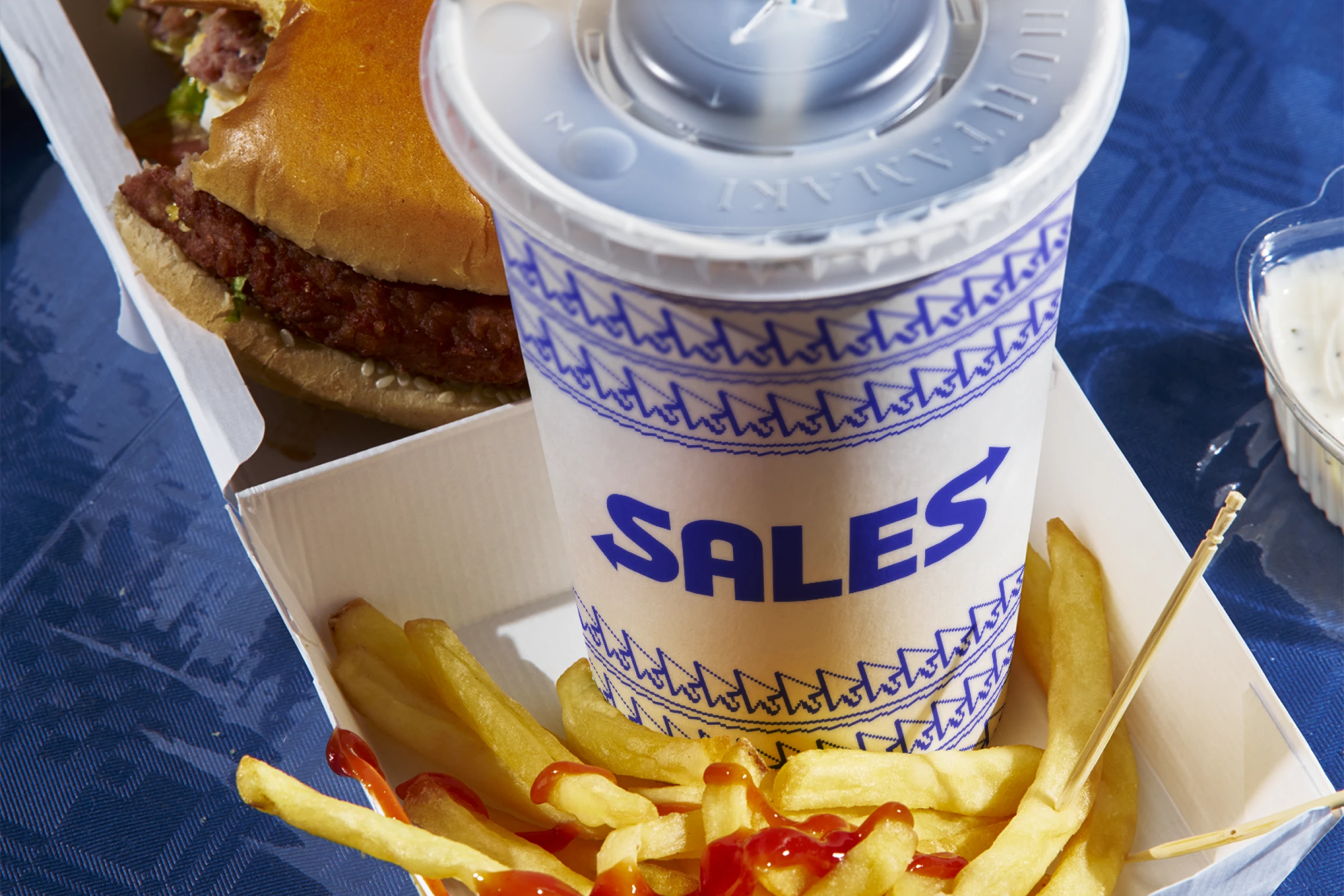 A drink cup sitting inside a burger box with a logo that says 'Sales'