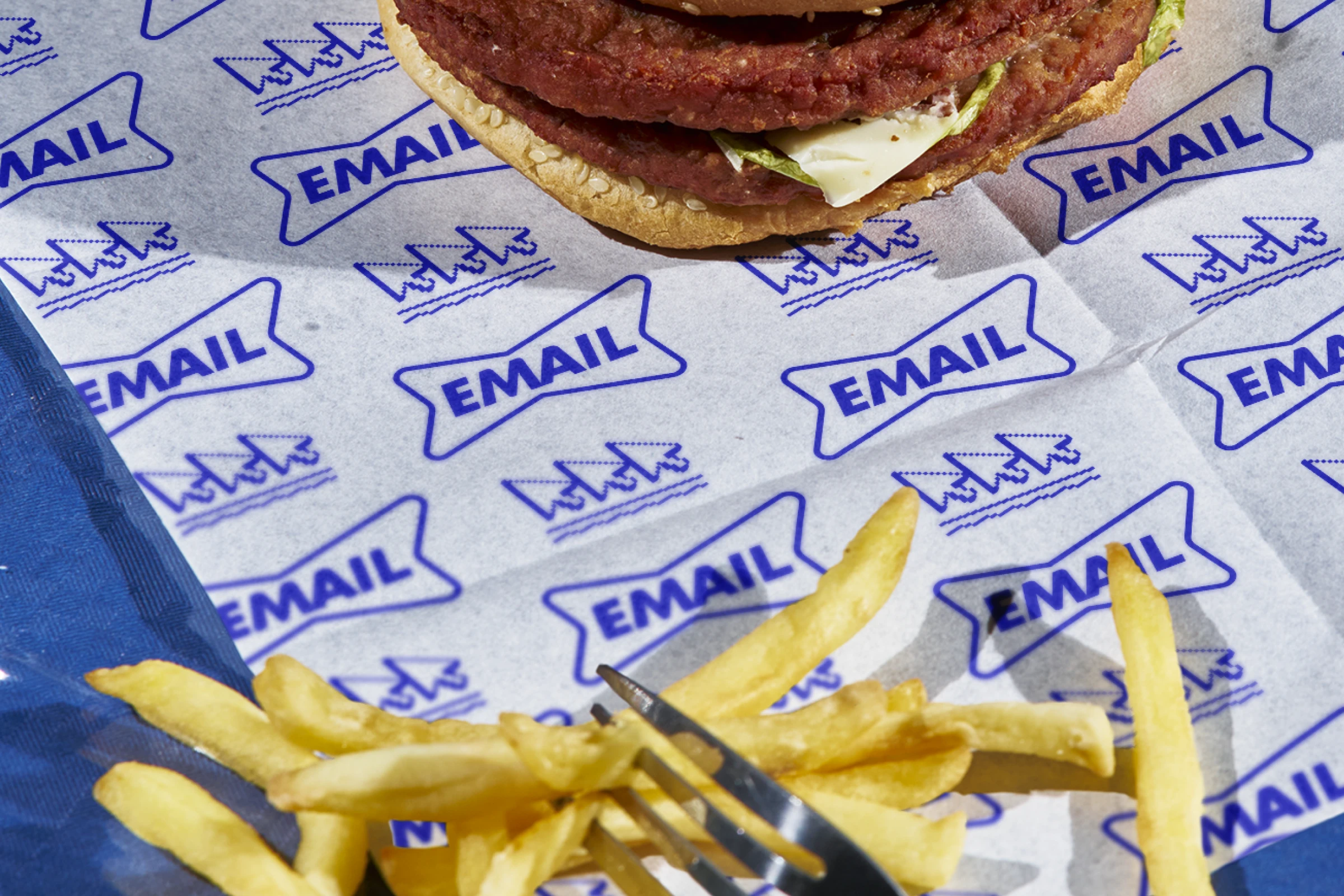 A burger wrapper with an 'email' logo repeated on it, with fries and a burger in shot