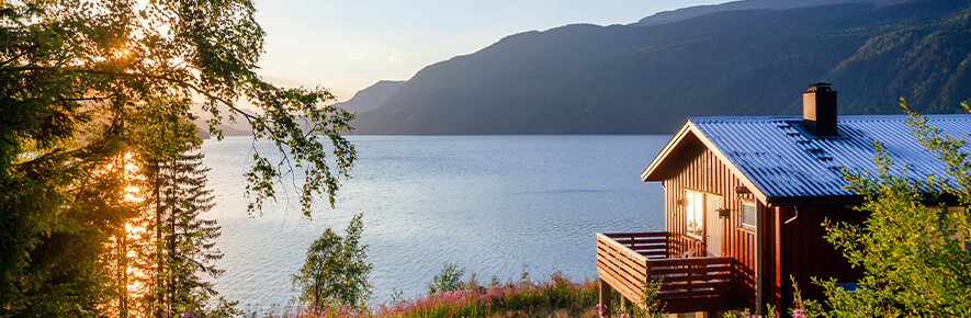 A Scandi-style lodge sits beside a vast lake surrounded by trees.
