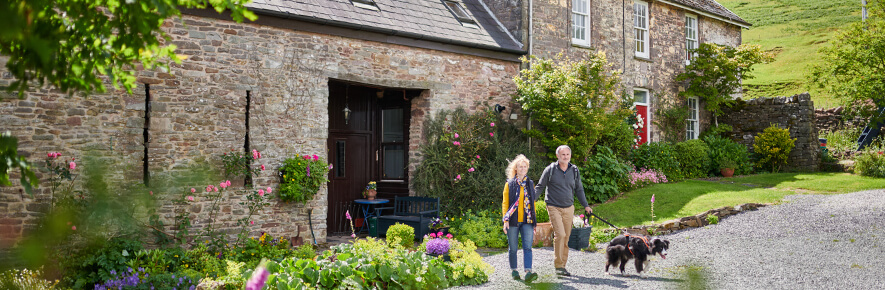 Two holidaymakers step out of a cottage with their dog on the lead. 