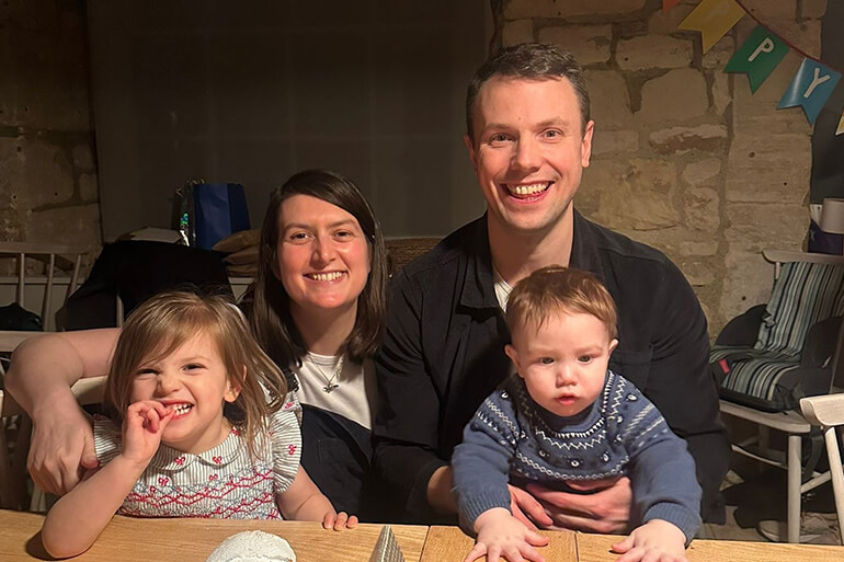 A young family, which includes two young children, smile at the camera from inside a stone-built cottage.