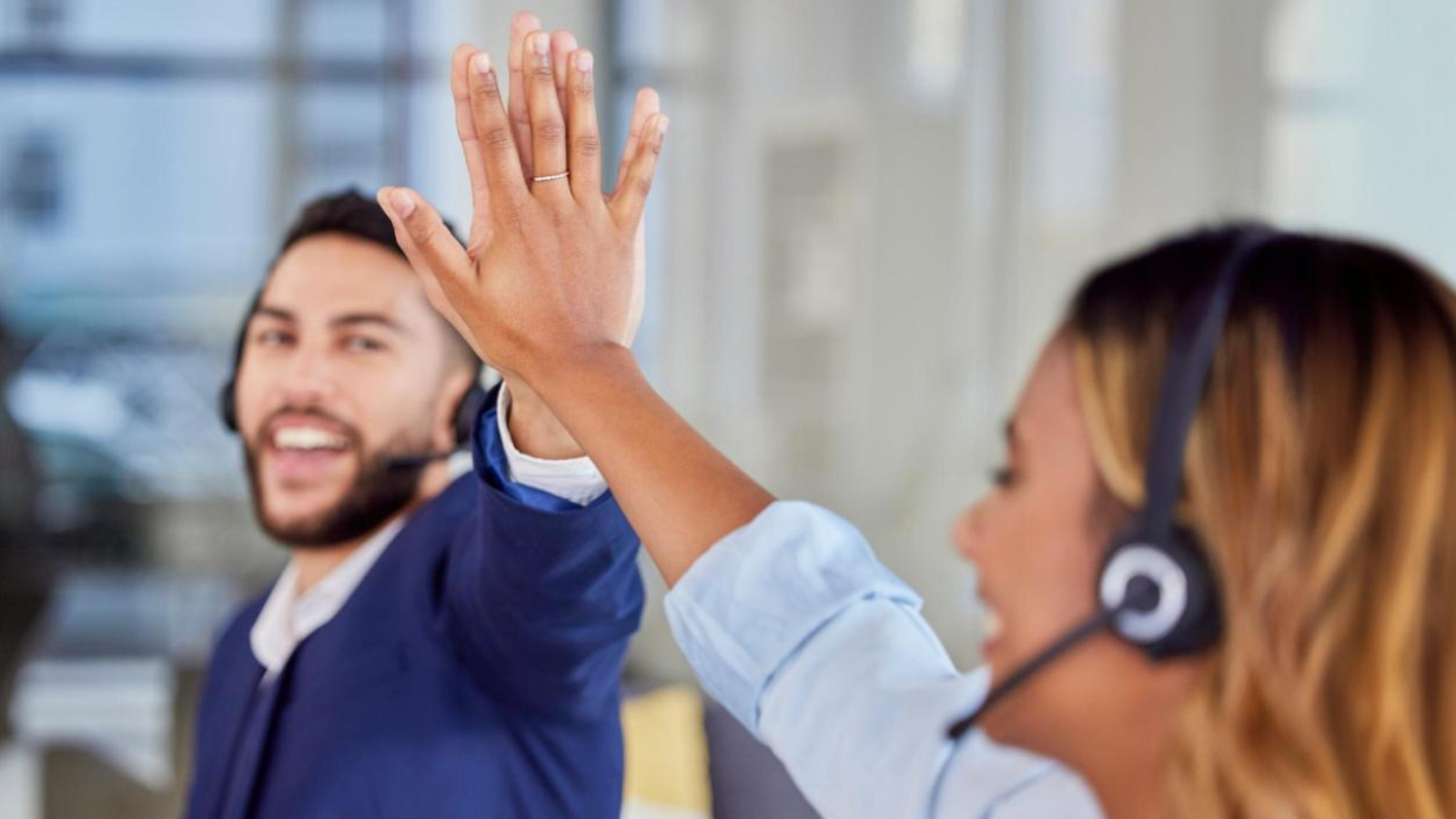 Two contact center agents wearing headsets high-five, showing seamless communication tools and improved customer relationships.