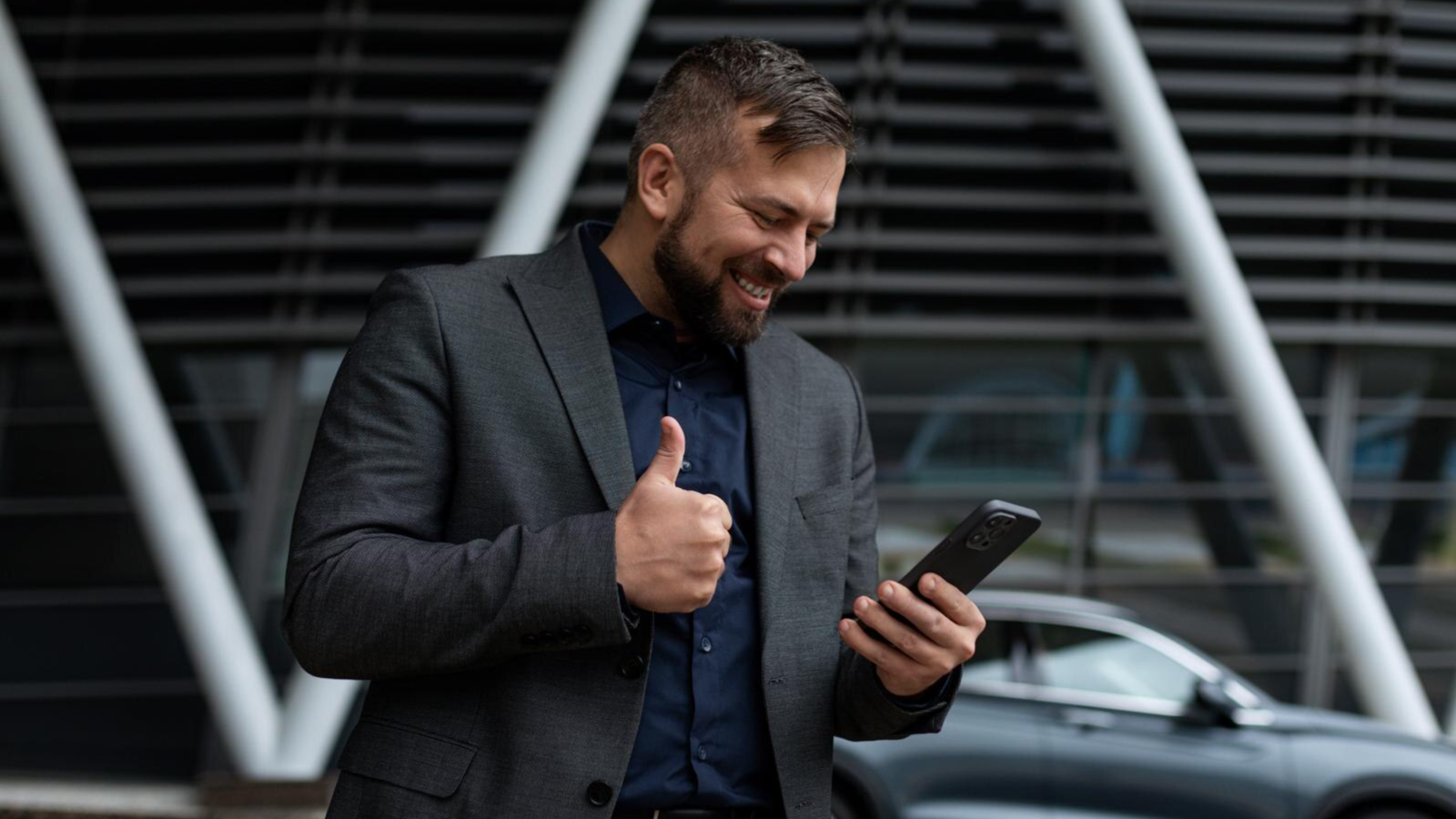 Smiling man outdoors giving a thumbs-up while viewing his phone, reflecting satisfaction with a cloud PBX phone system.