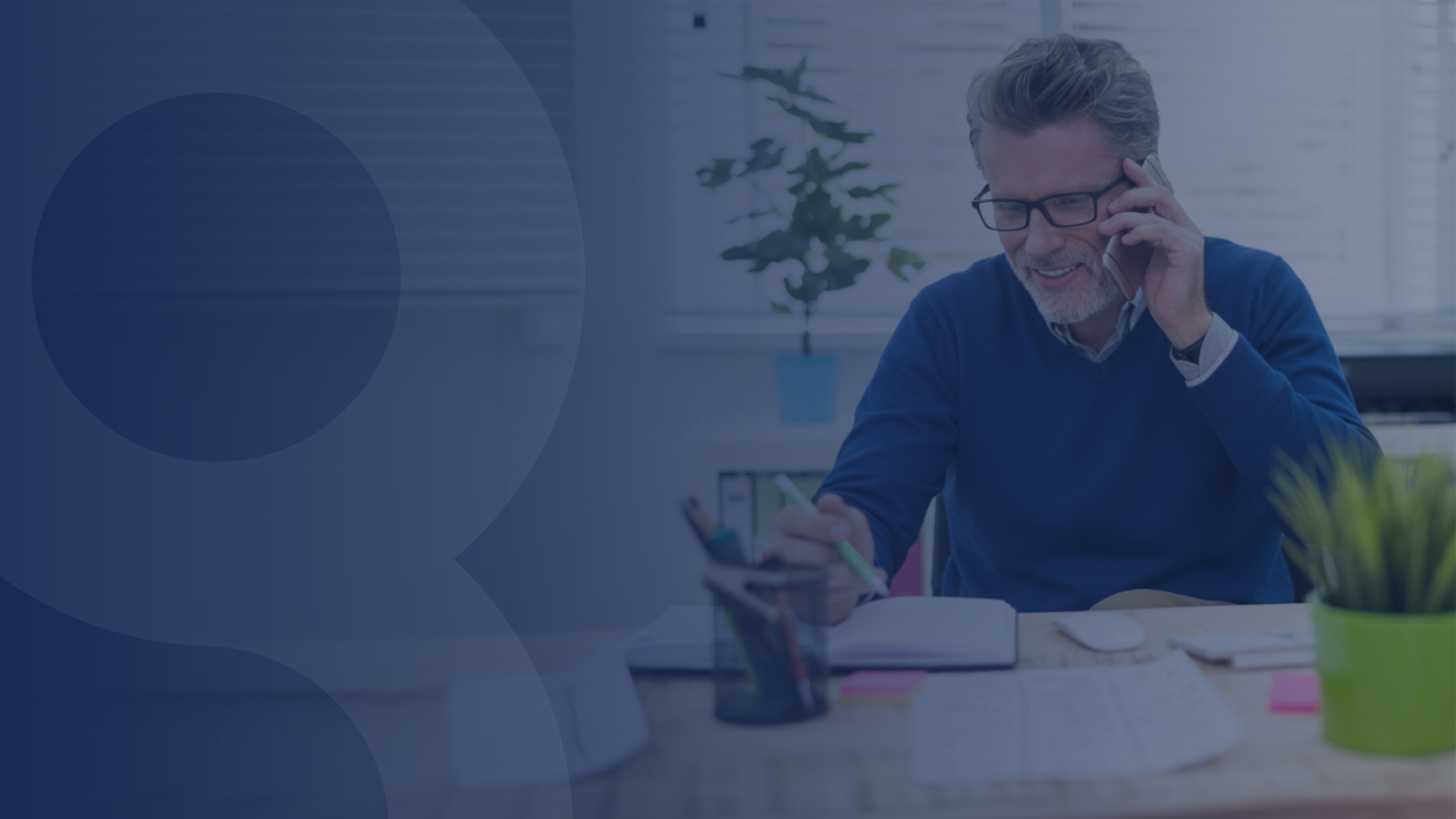 Smiling man on a phone call while writing at his desk, representing effective communication with UCaaS solutions.