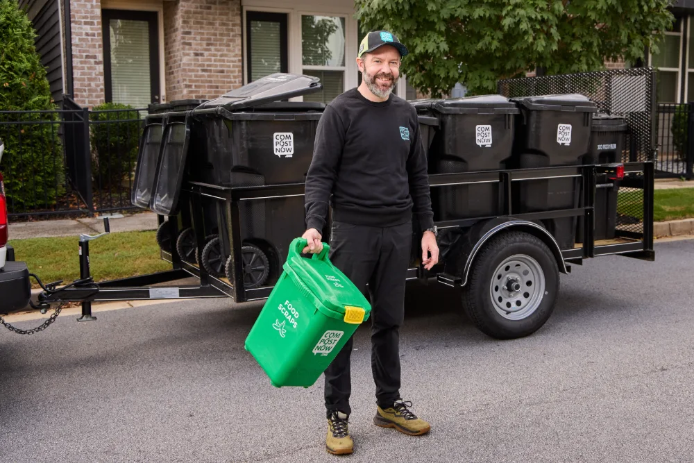 CompostNow crew member carrying a green food scraps bin on a residential street