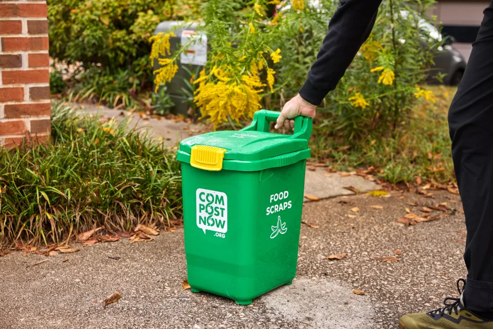 Green food scraps bin set down at the curb in front of a home's garden