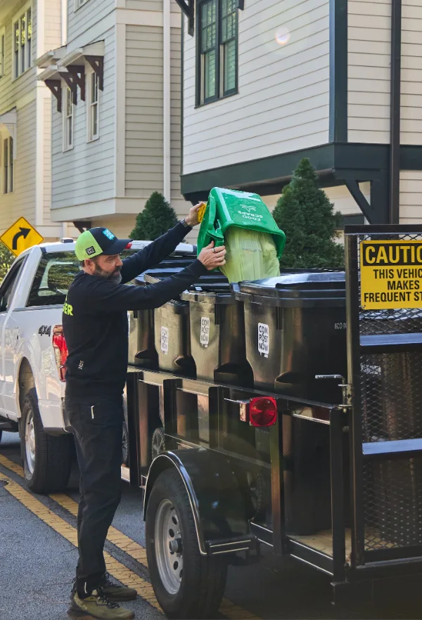 CompostNow crew member emptying a green food scraps bin into a cart on the collection trailer outside townhomes