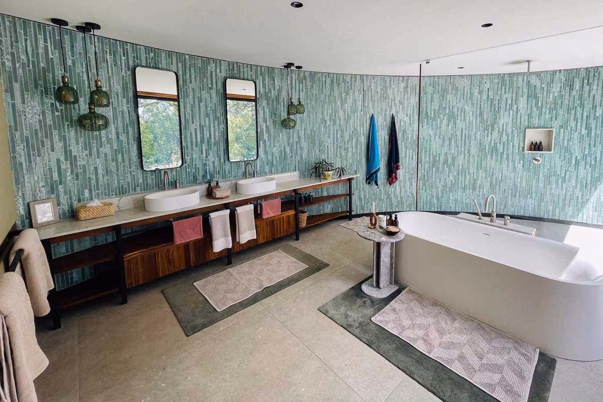 Spacious bathroom with freestanding tub, double sink vanity, green tile wall, and hanging pendant lights.