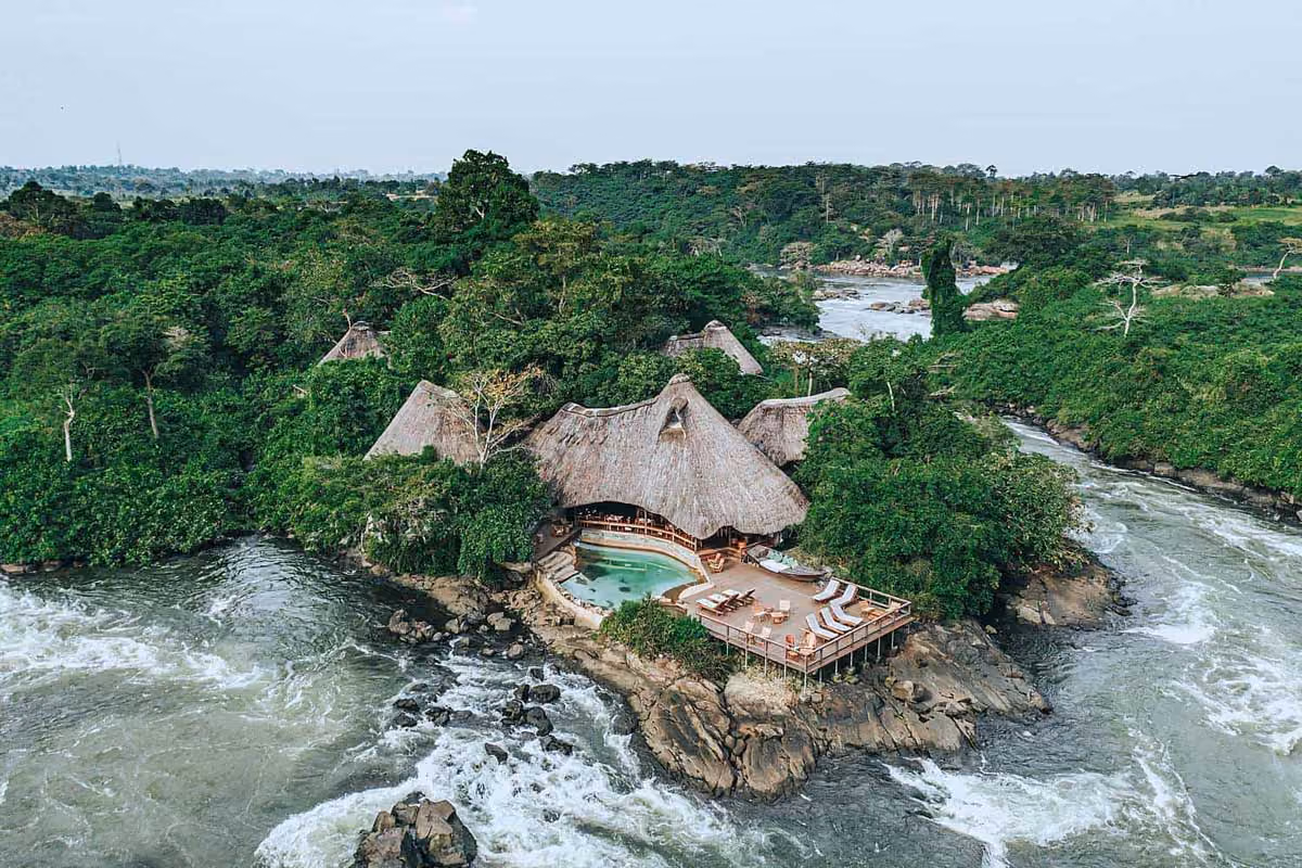 Thatched-roof lodge with pool and deck surrounded by lush greenery on a rocky river bend.