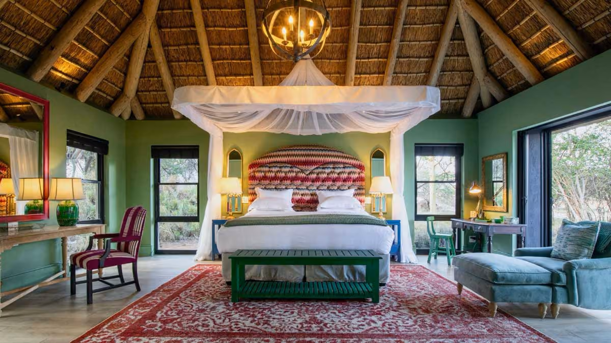 Spacious bedroom with high thatched ceiling, patterned headboard bed, green walls, and large windows.