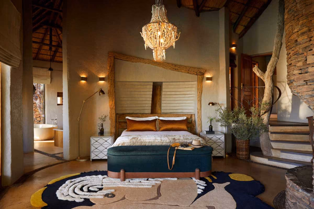 Cozy bedroom with wooden frame bed, orange pillows, chandelier, patterned rug, and natural decor elements.