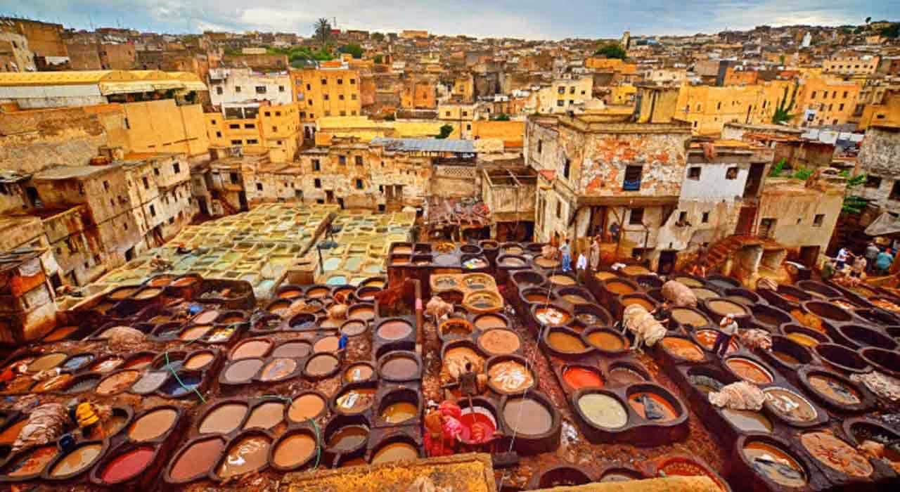 A traditional leather tannery with large colorful dyeing vats and workers in an old city setting.