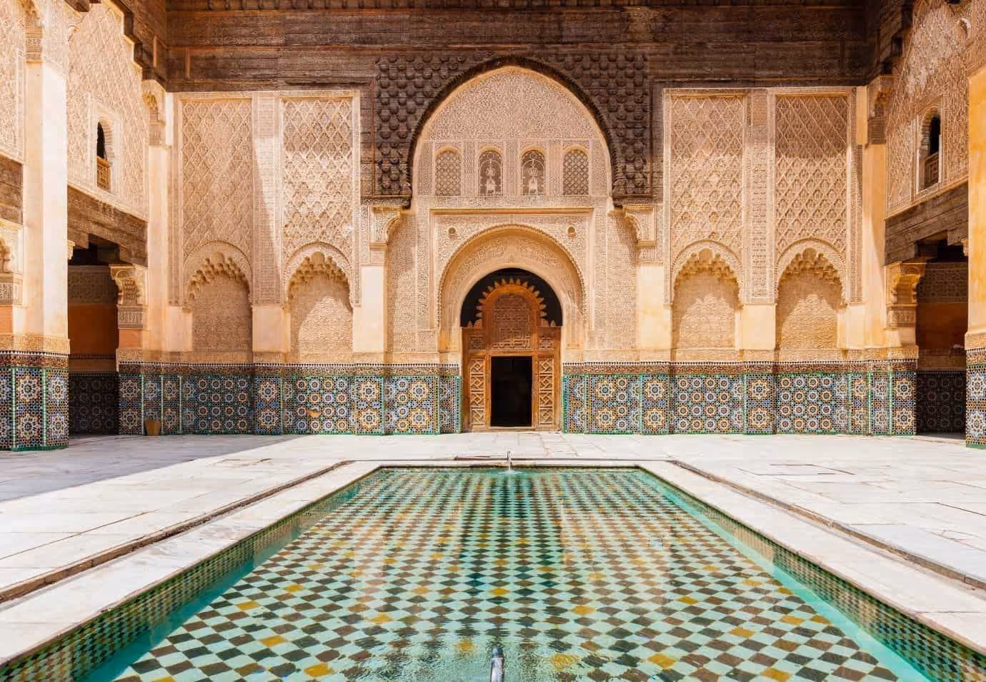 Ornate courtyard with colorful mosaic pool and intricate carved walls in historic Islamic architecture.