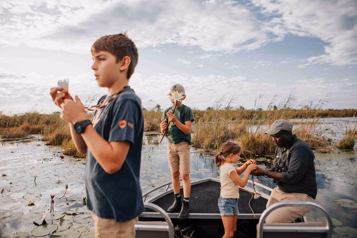 Two boys and a girl with a man on a boat in a marsh holding white flowers at sunset.