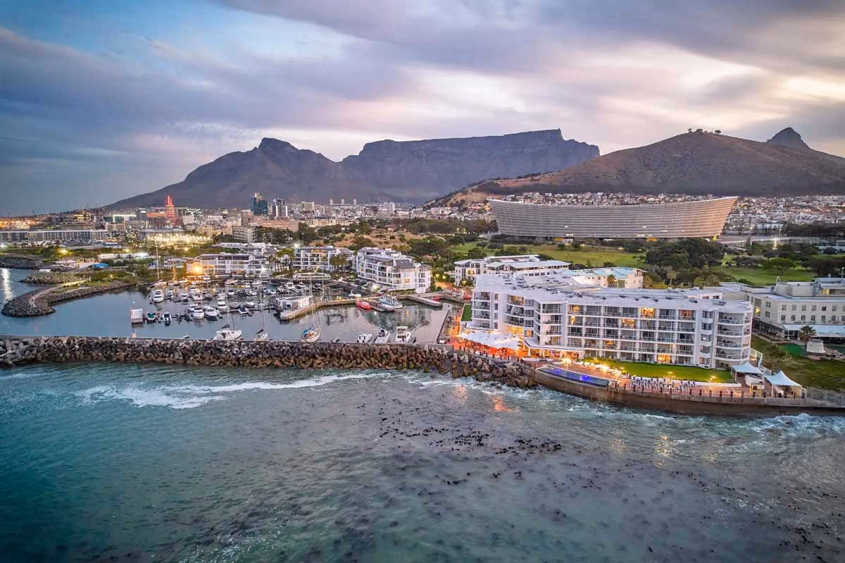 Aerial view of Cape Town harbor, tables, and buildings with Table Mountain in the background at dusk.