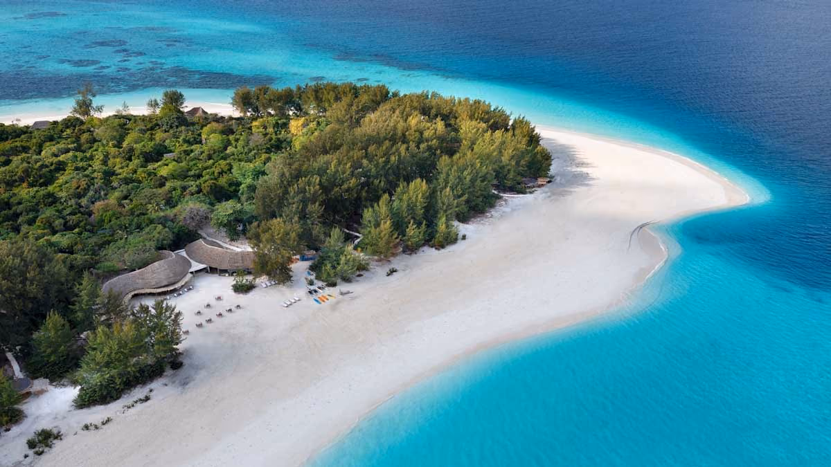 Aerial view of a tropical island with white sandy beach, turquoise water, and green trees.