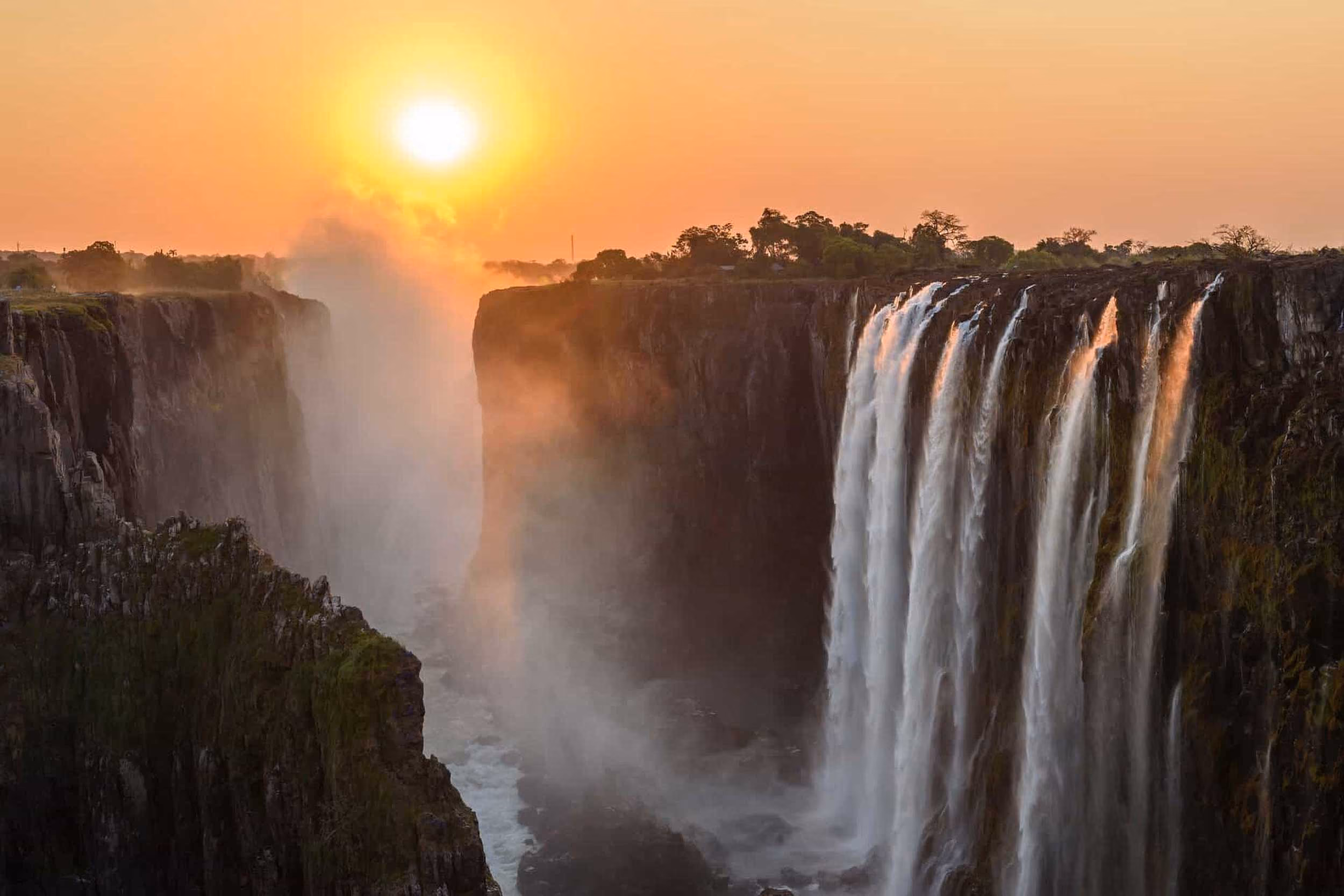 Victoria Falls at sunset with mist and water cascading over high cliffs.