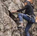 Person wearing a helmet and climbing gear ascending a rocky cliff.