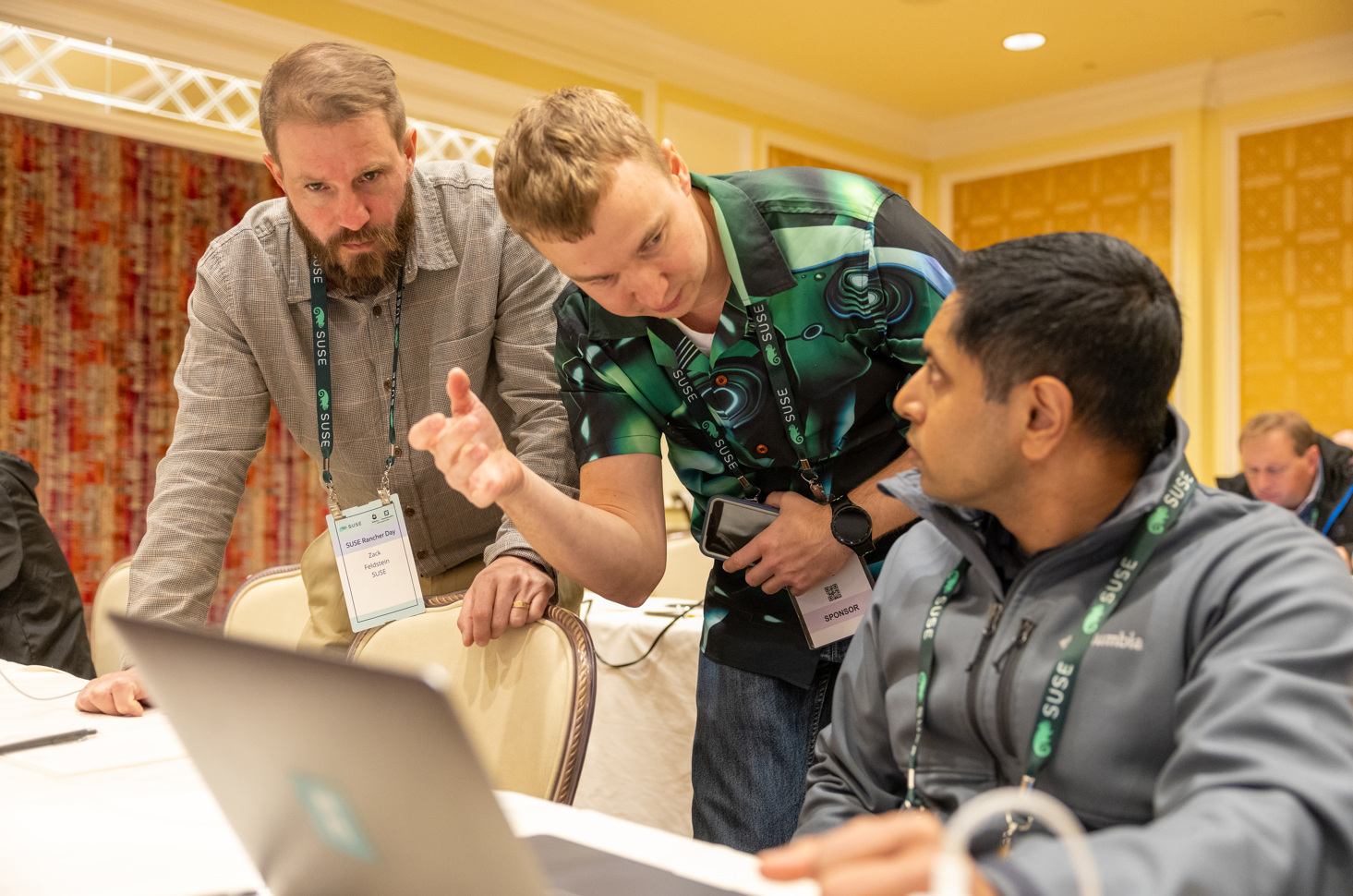 Three people talking in front of a computer at Suse KubeCon