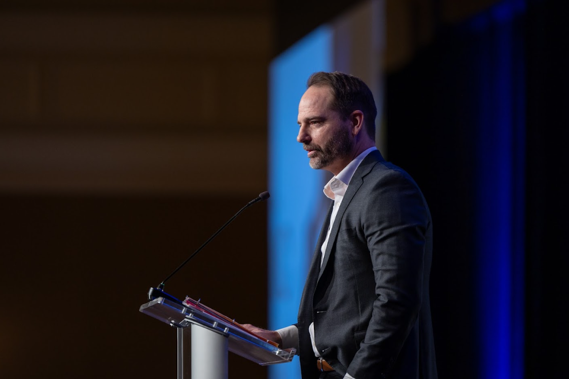 One man in front of a podium on stage giving a speech
