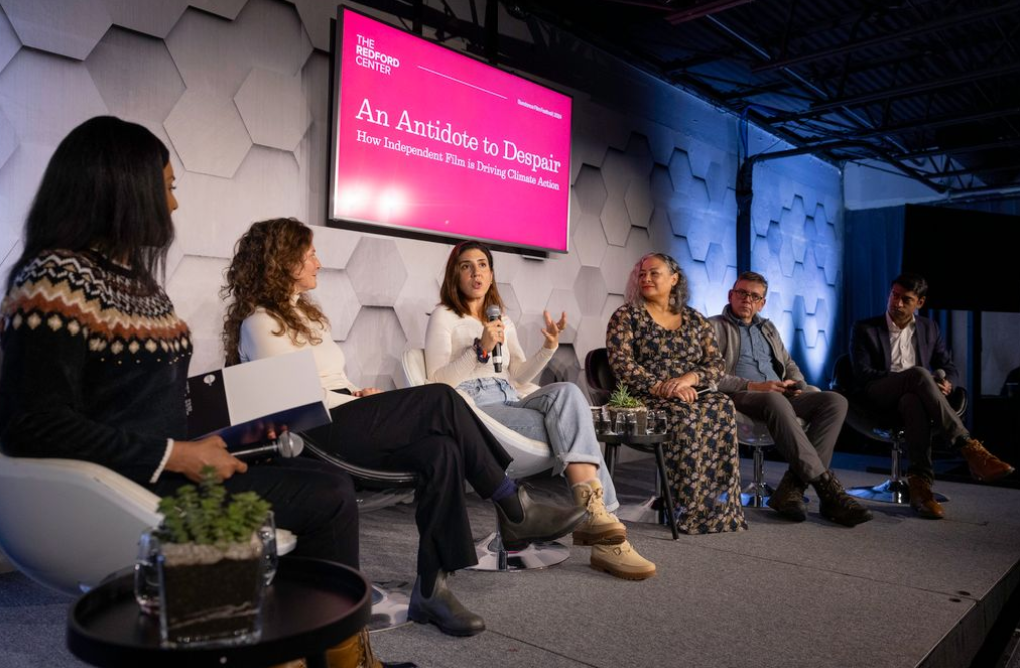 Several women and two men on stage at a panel event speaking