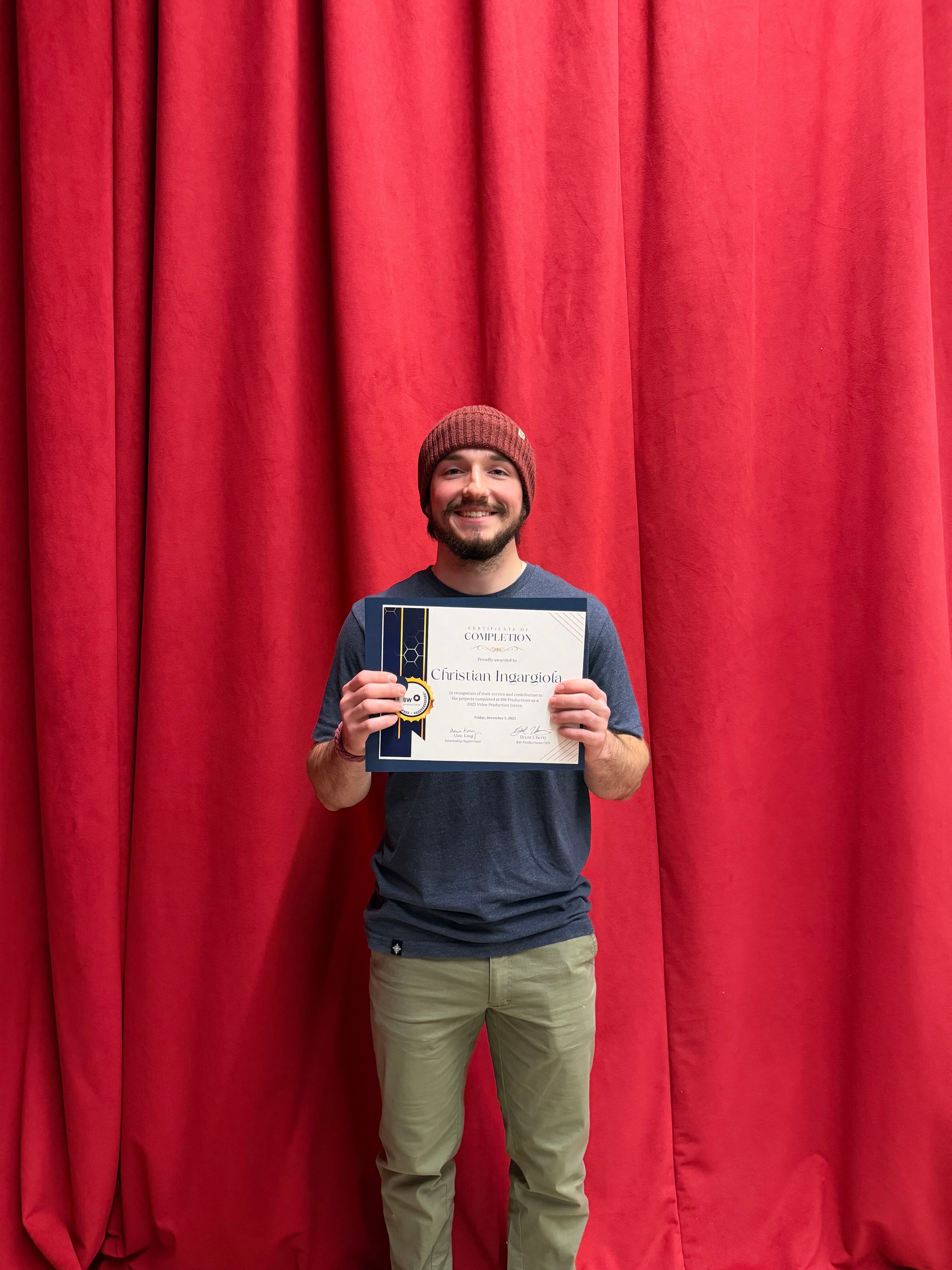 Man holding internship completion certificate in front of red curtain