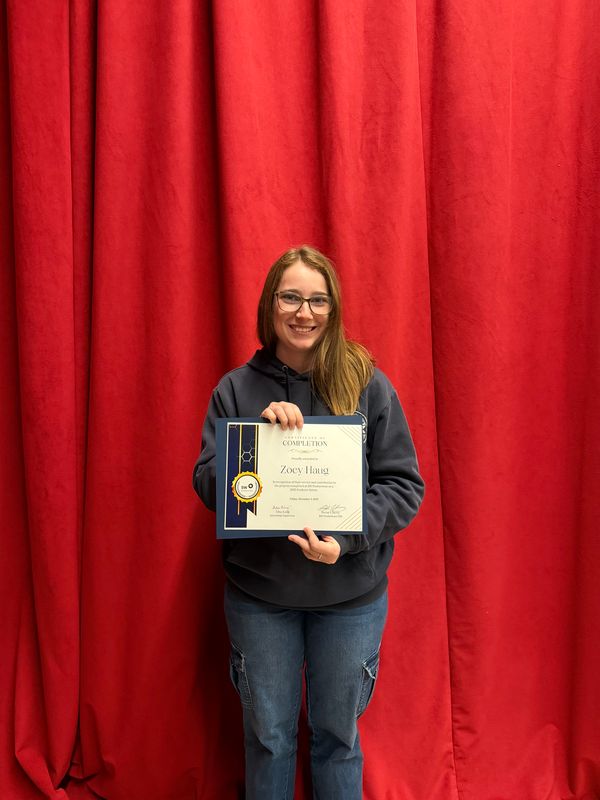 Woman in front of red curtain holding internship completion certificate