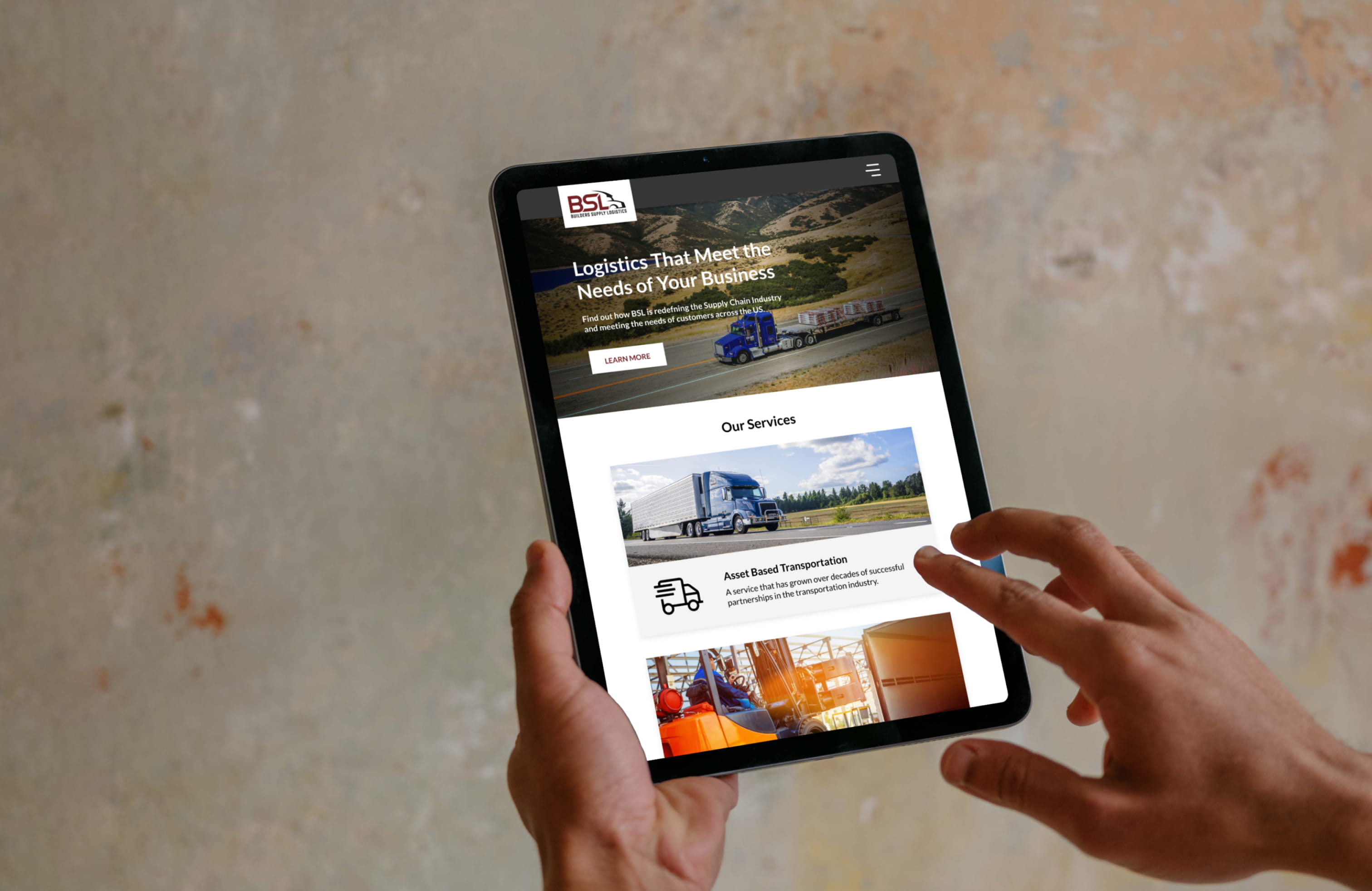 A tablet being held in portrait mode, displaying the BSL home page, as the user scrolls.