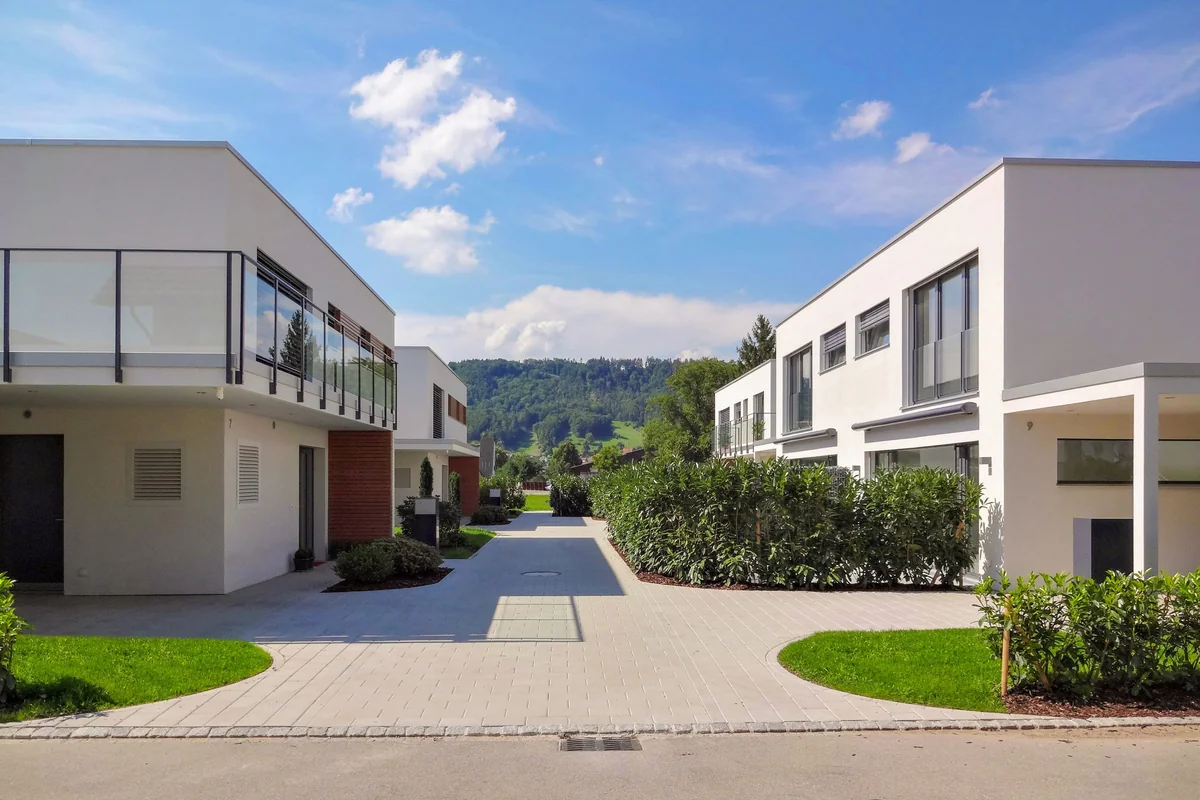 Einfamilienhäuser Lommis: gemeinsame Zufahrt zwischen den weissen Flachdachhäusern mit Blick zum Waldhang