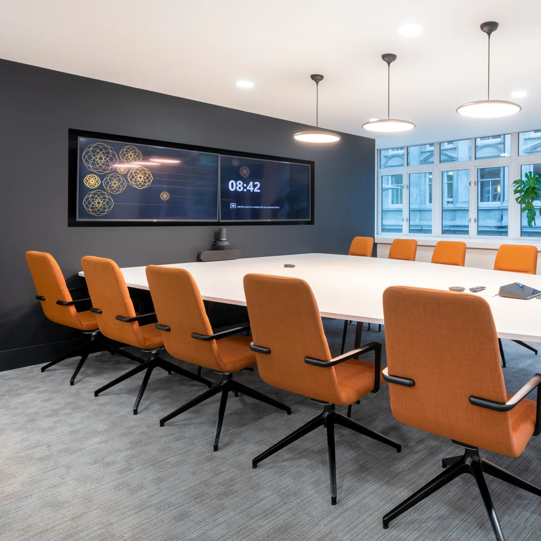 A conference room with a large white table and orange chairs.